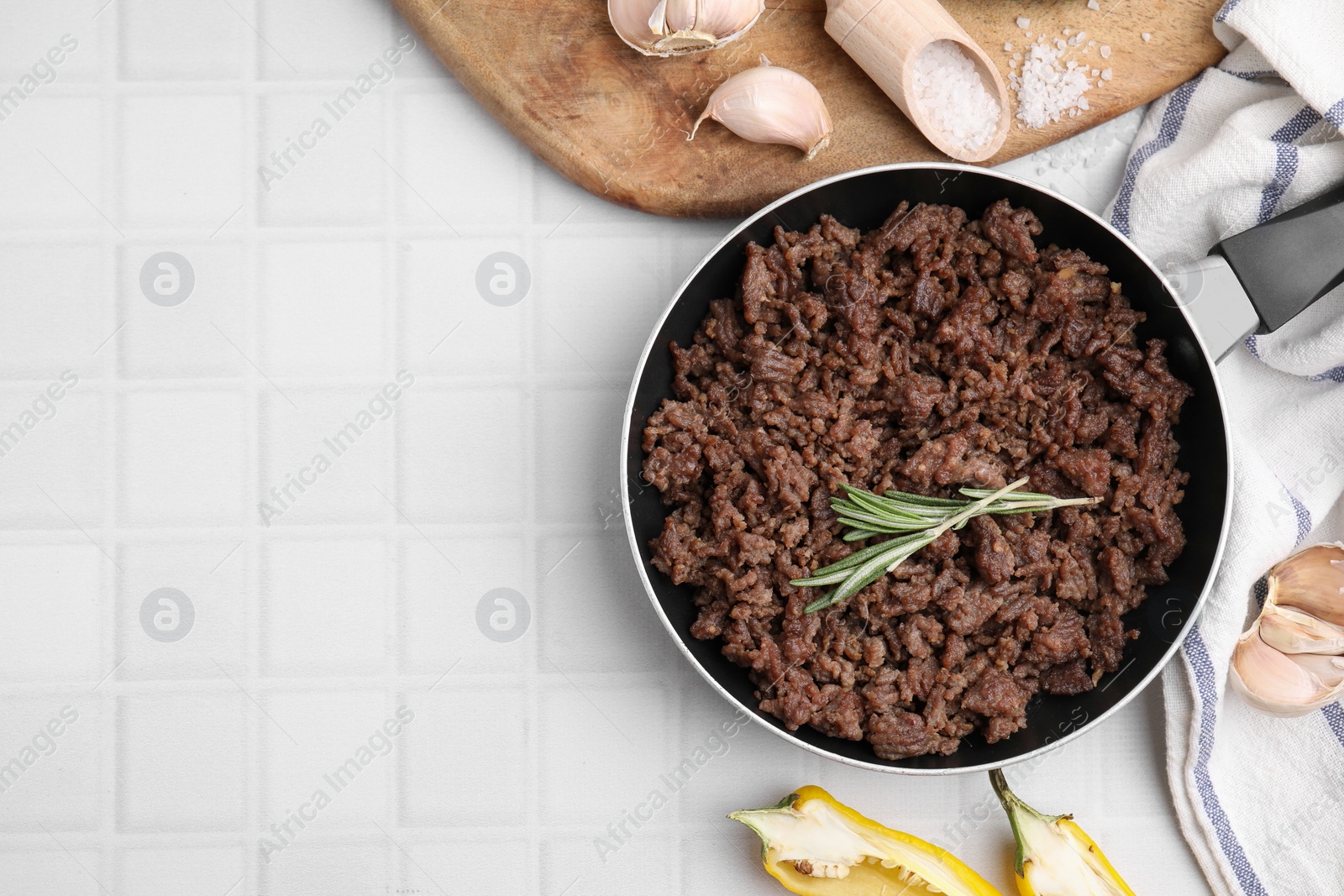 Photo of Fried ground meat in frying pan and products on white tiled table, flat lay. Space for text