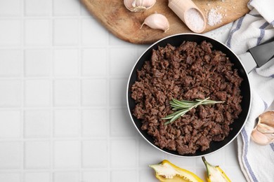 Photo of Fried ground meat in frying pan and products on white tiled table, flat lay. Space for text
