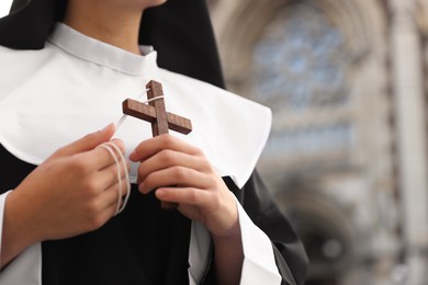 Photo of Young nun with Christian cross near cathedral outdoors, closeup. Space for text