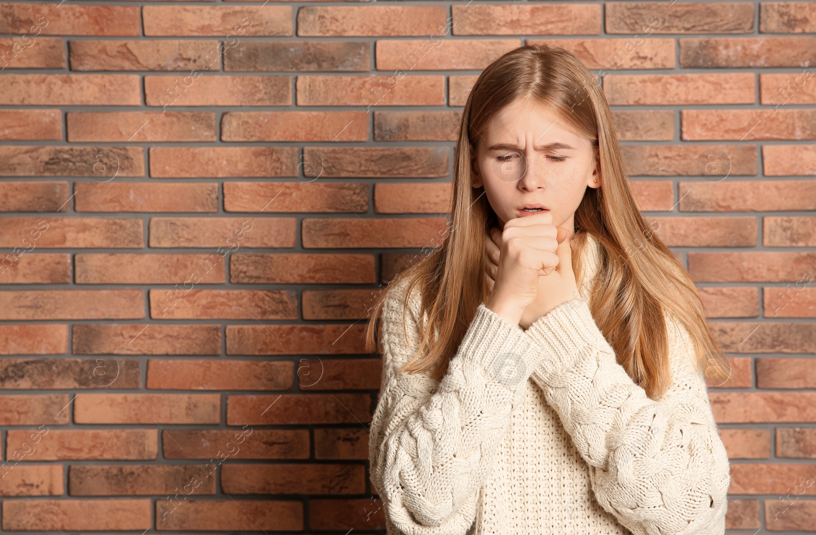 Photo of Teenage girl suffering from cough near brick wall. Space for text
