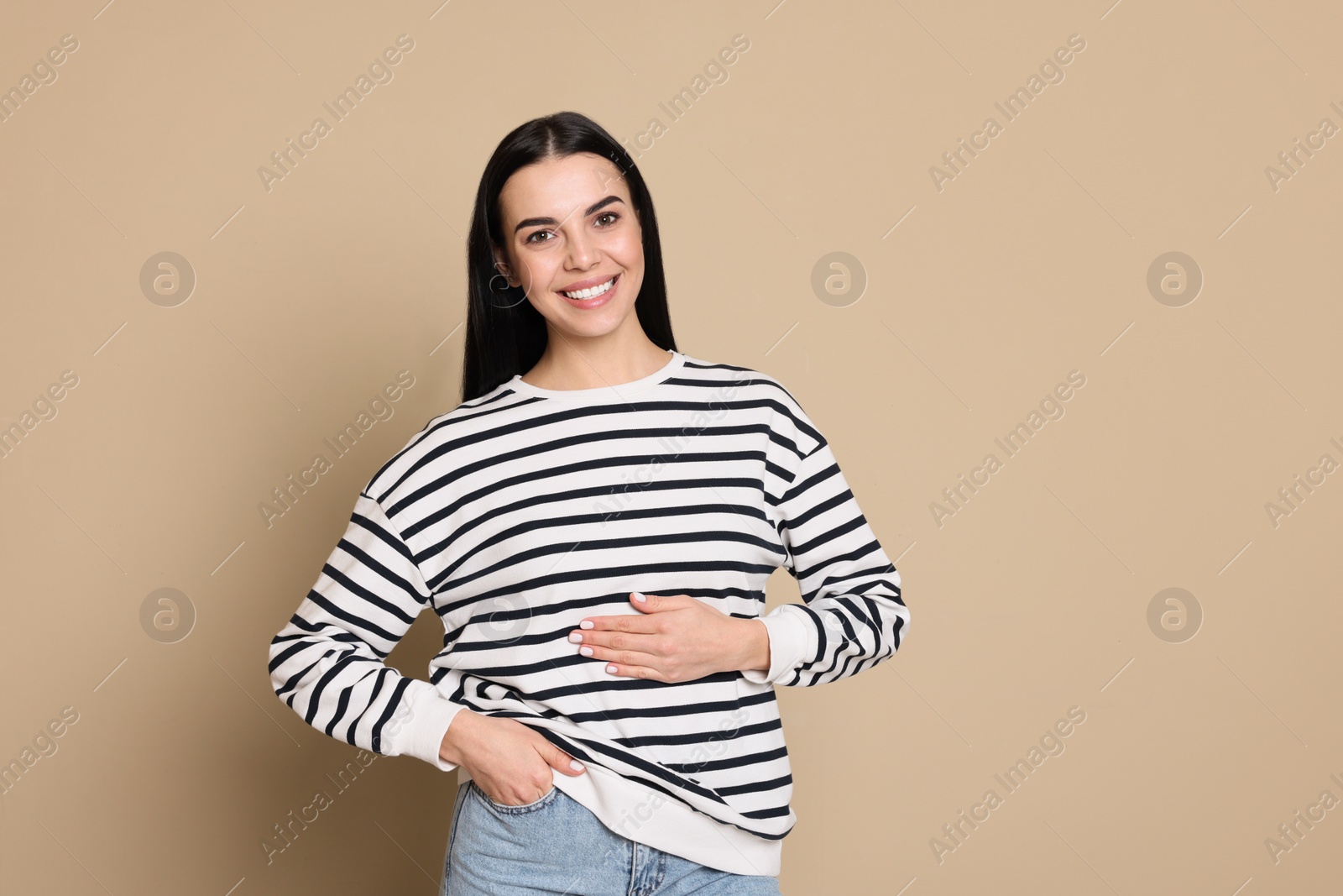 Photo of Happy healthy woman touching her belly on beige background