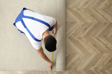 Photo of Worker with measuring tape installing new carpet indoors, top view