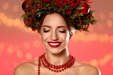 Beautiful young woman wearing Christmas wreath against blurred festive lights, closeup