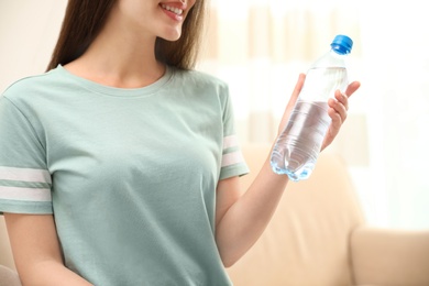 Woman with bottle of fresh water indoors, closeup