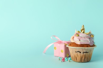 Photo of Cute sweet unicorn cupcake and gift box on light turquoise background, space for text