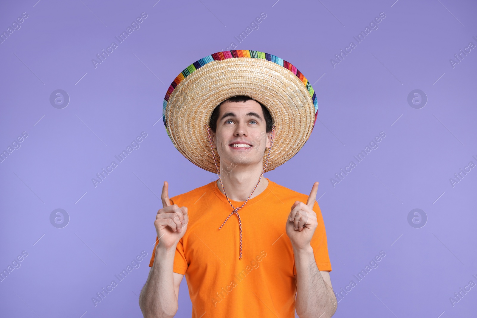 Photo of Young man in Mexican sombrero hat pointing at something on violet background