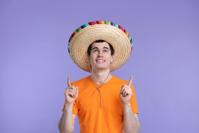 Photo of Young man in Mexican sombrero hat pointing at something on violet background