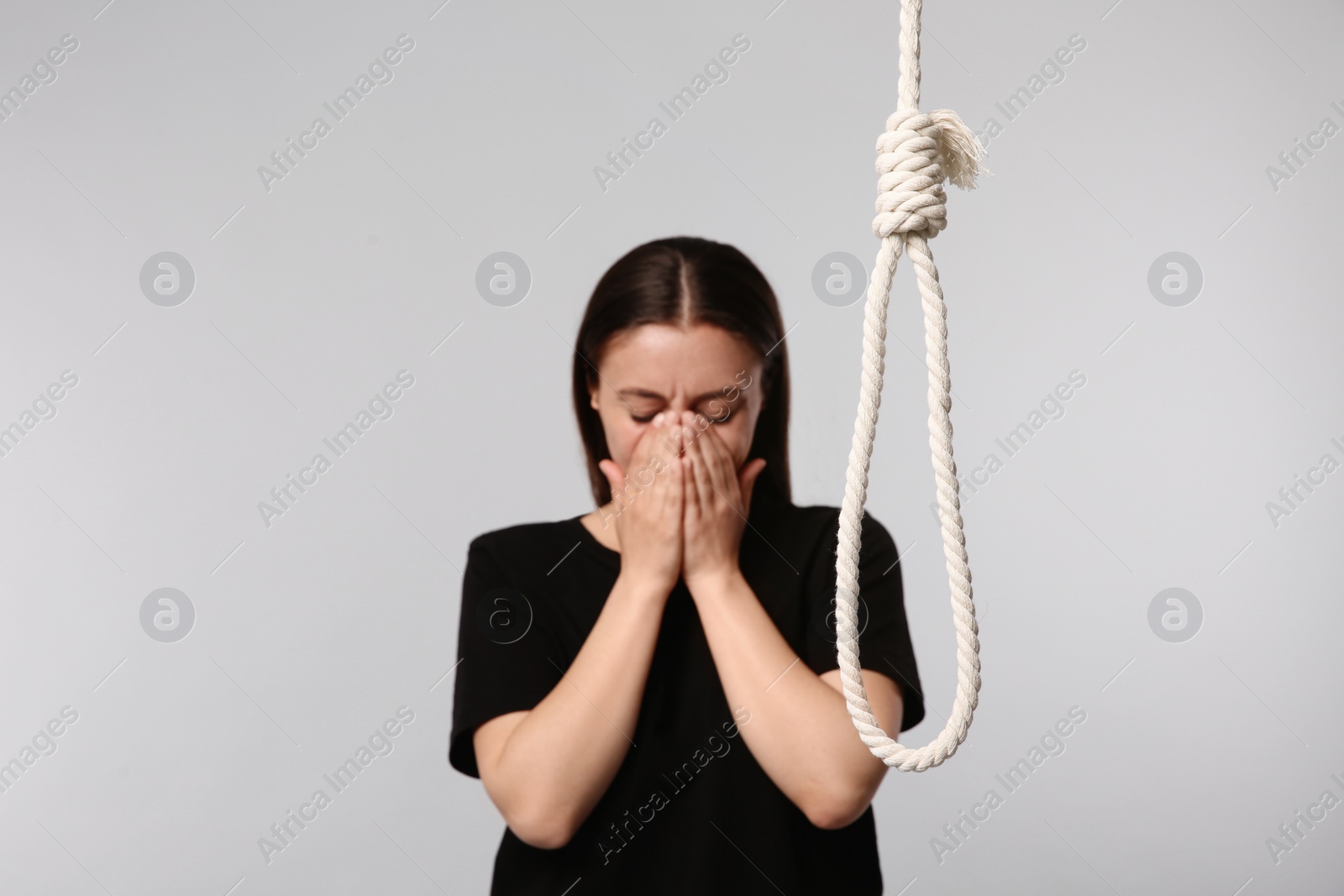 Photo of Depressed woman crying near rope noose on light grey background