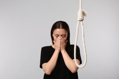 Depressed woman crying near rope noose on light grey background