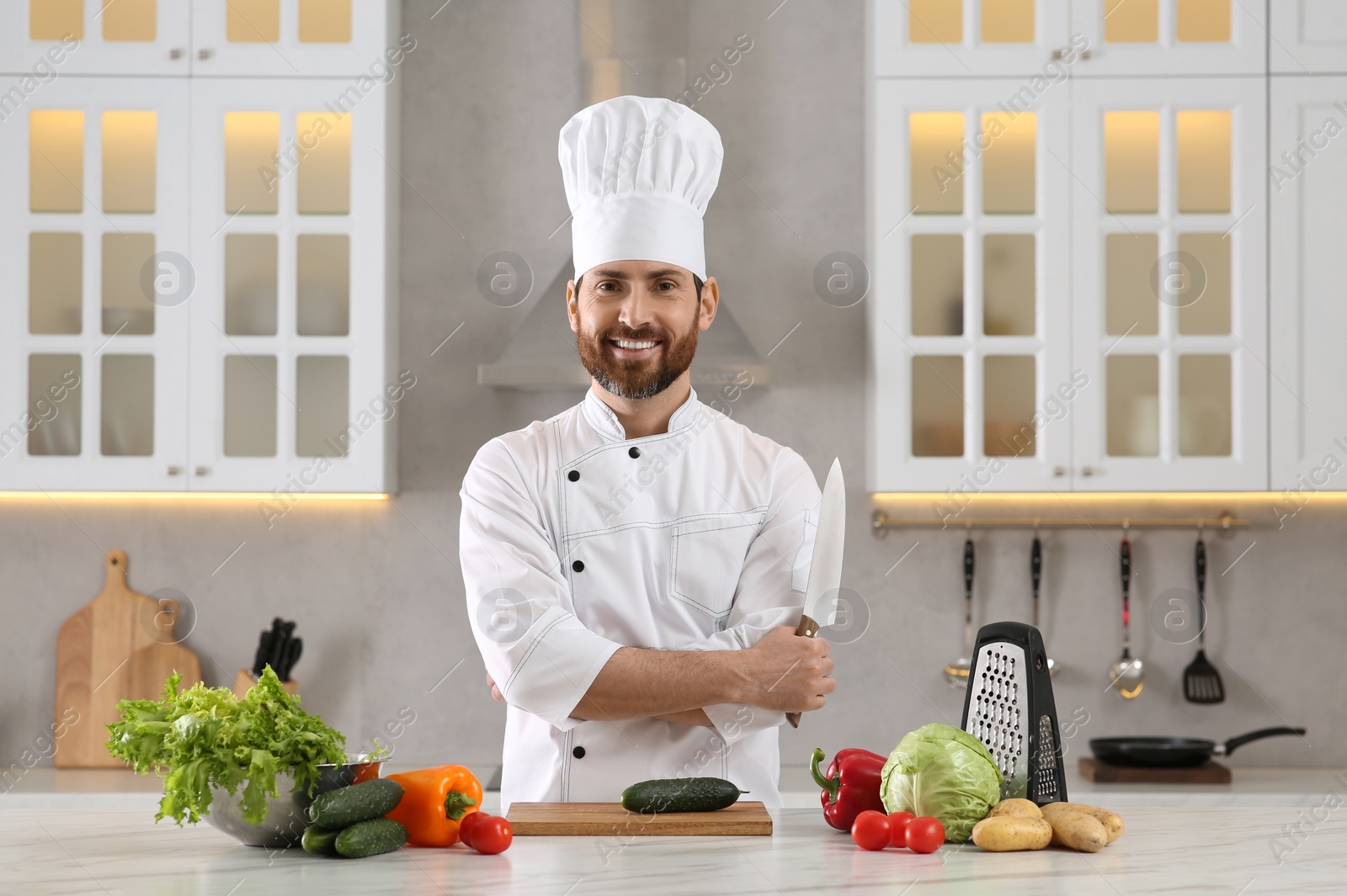 Photo of Portrait of happy chef with knife at marble table in kitchen