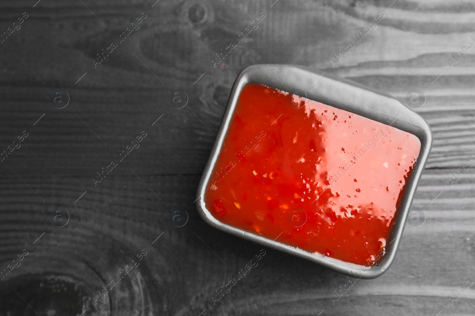 Photo of Spicy chili sauce in bowl on black wooden table, top view. Space for text