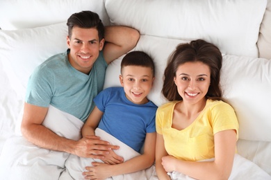 Portrait of happy young family resting in bed, above view