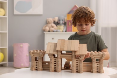 Little boy playing with wooden entry gate at white table in room, space for text. Child's toy