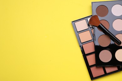 Different contouring palettes and brush on yellow background, flat lay with space for text. Professional cosmetic product