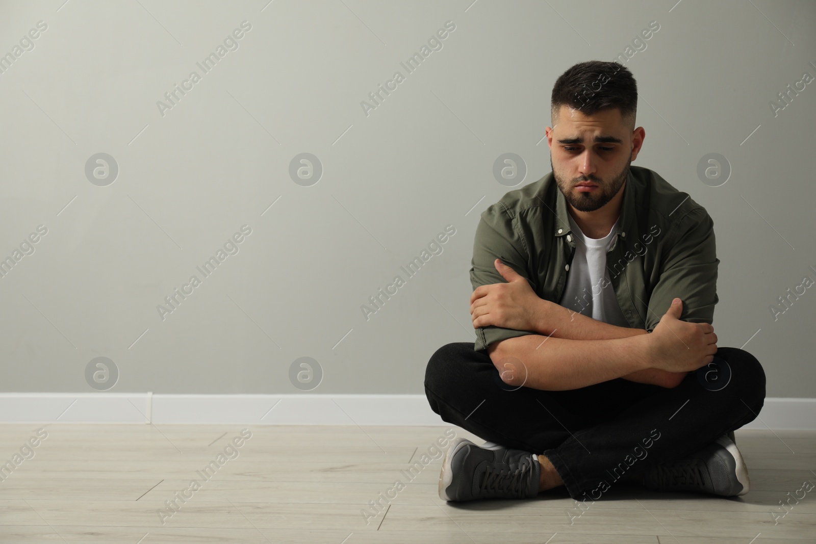 Photo of Sad man sitting on floor near light grey wall. Space for text