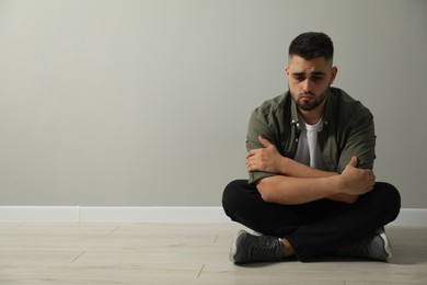 Sad man sitting on floor near light grey wall. Space for text