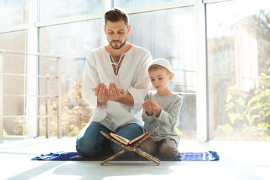 Photo of Muslim man and his son praying together indoors