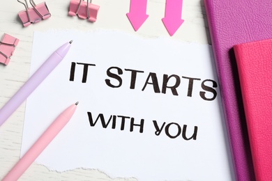Photo of Sheet of paper with phrase It Starts With You and stationery on white table, flat lay