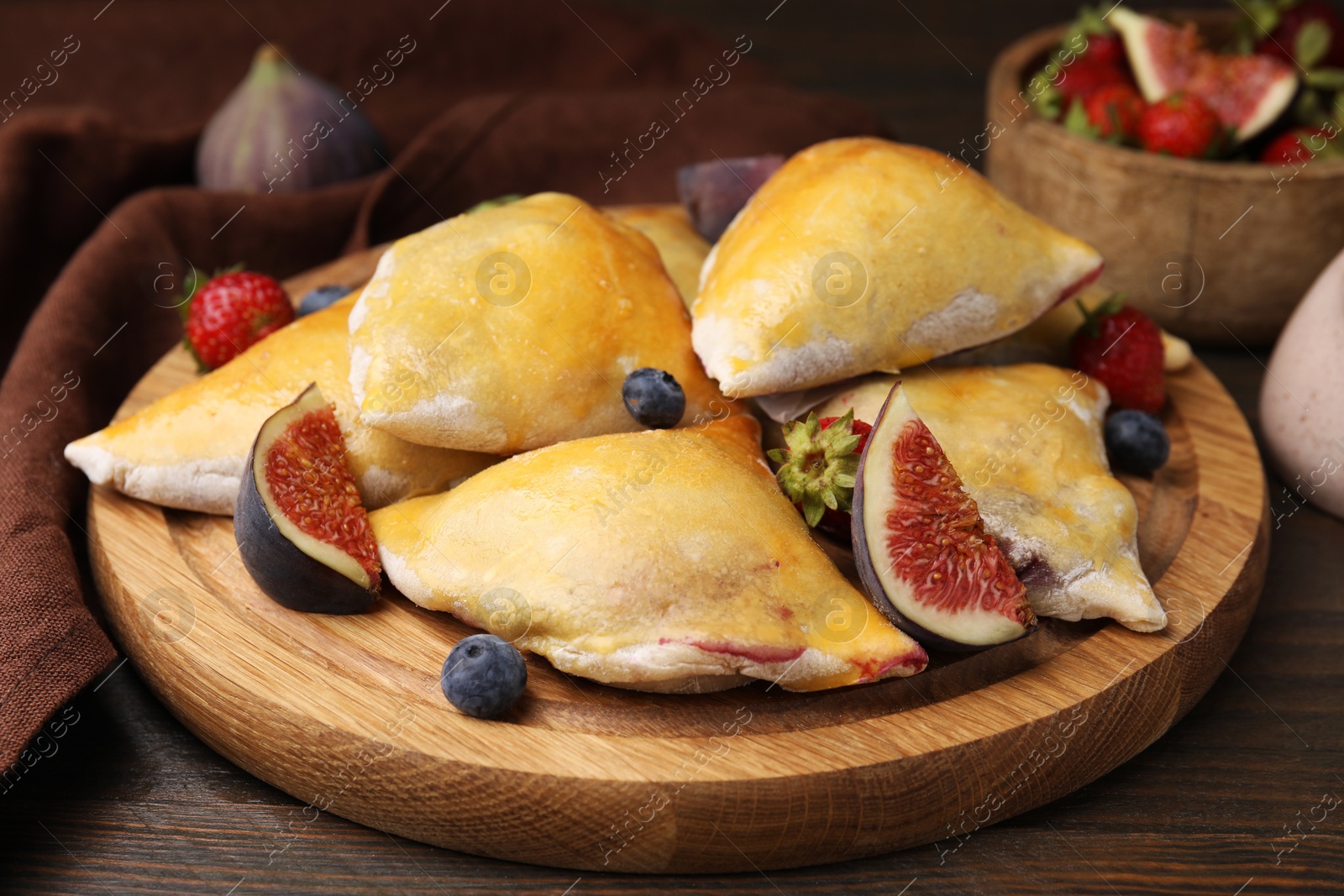 Photo of Delicious samosas with figs and berries on wooden table, closeup