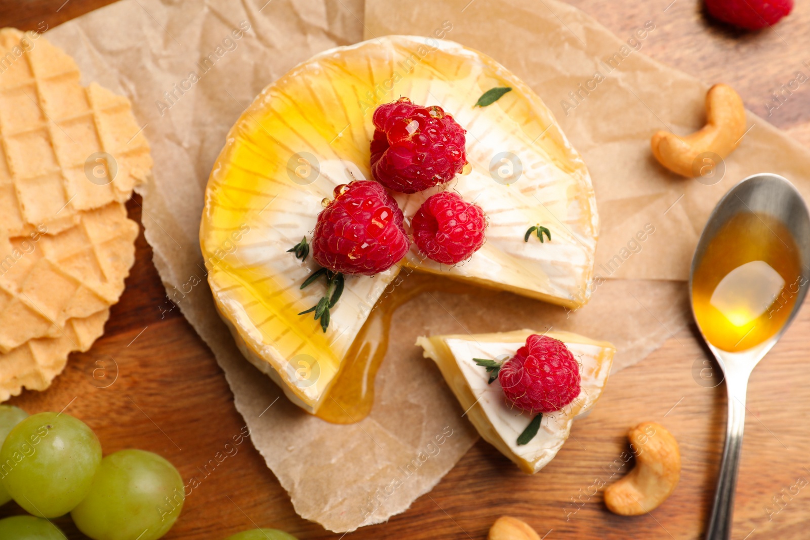 Photo of Brie cheese served with berries and honey on wooden table, flat lay