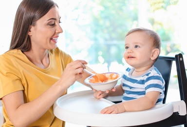 Photo of Woman feeding her child in highchair indoors. Healthy baby food
