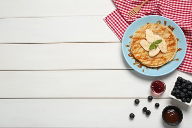 Photo of Delicious crepes with blueberries, mint, banana and jam on white wooden table, flat lay. Space for text