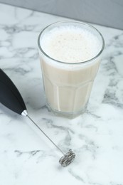 Mini mixer (milk frother) and tasty cappuccino in glass on white marble table