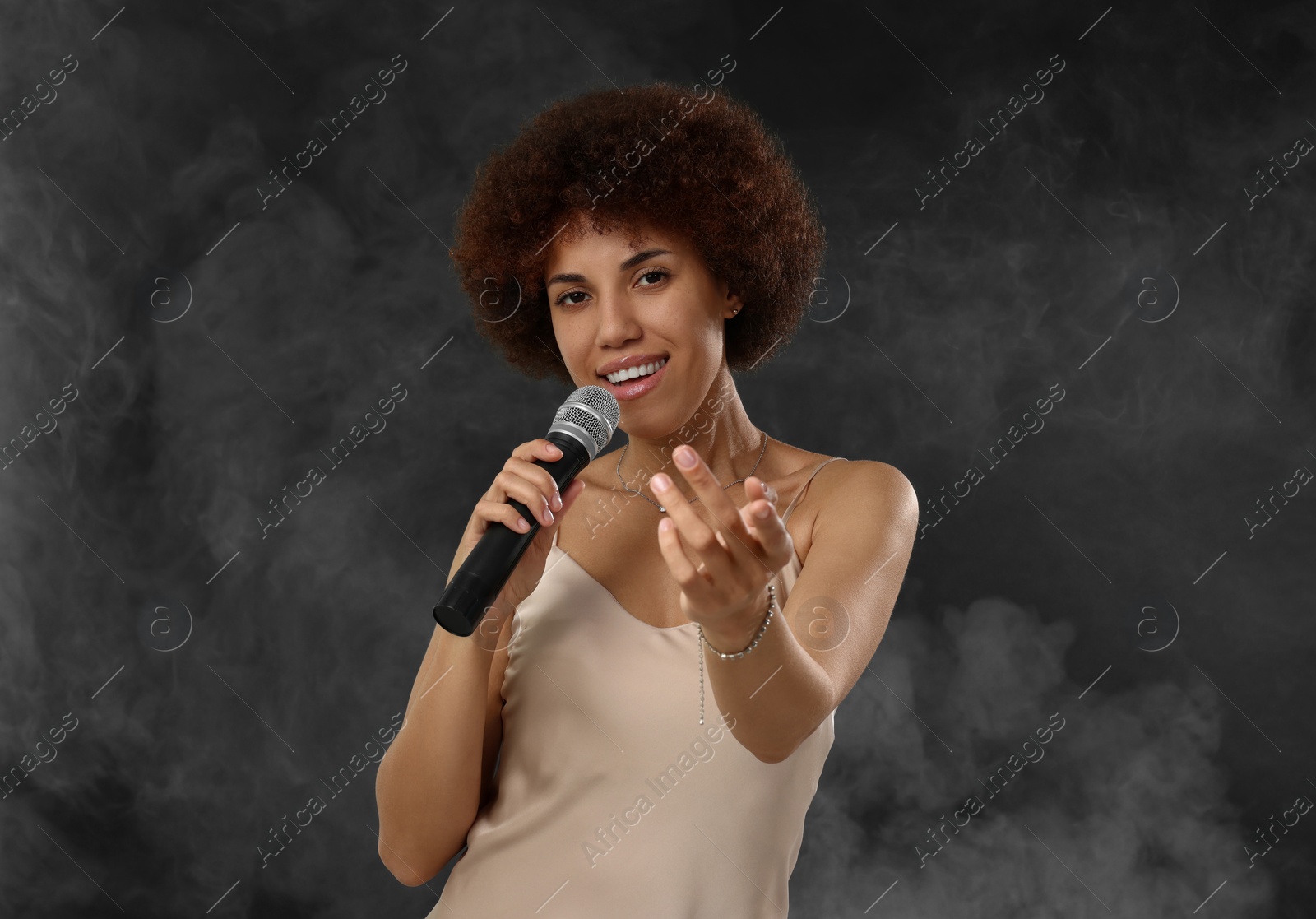 Photo of Curly young woman with microphone singing in smoke on black background