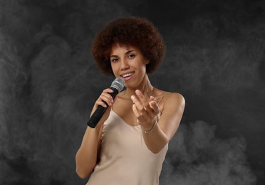 Curly young woman with microphone singing in smoke on black background