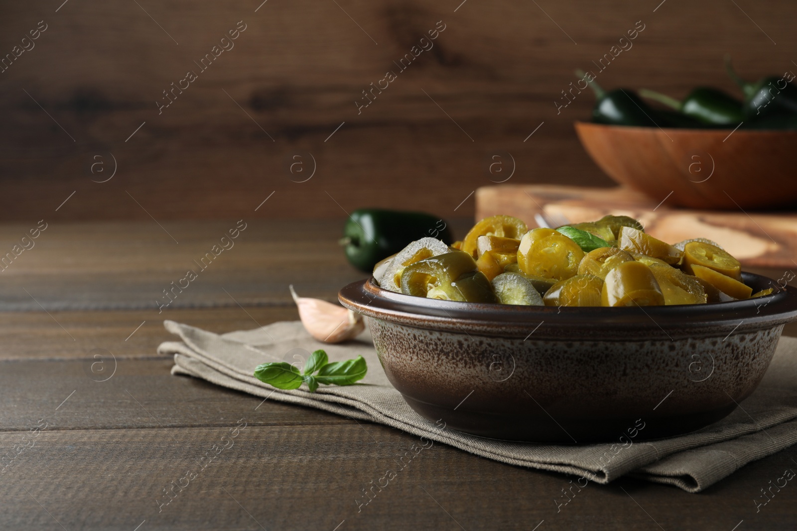 Photo of Bowl with slices of pickled green jalapeno peppers on wooden table, space for text