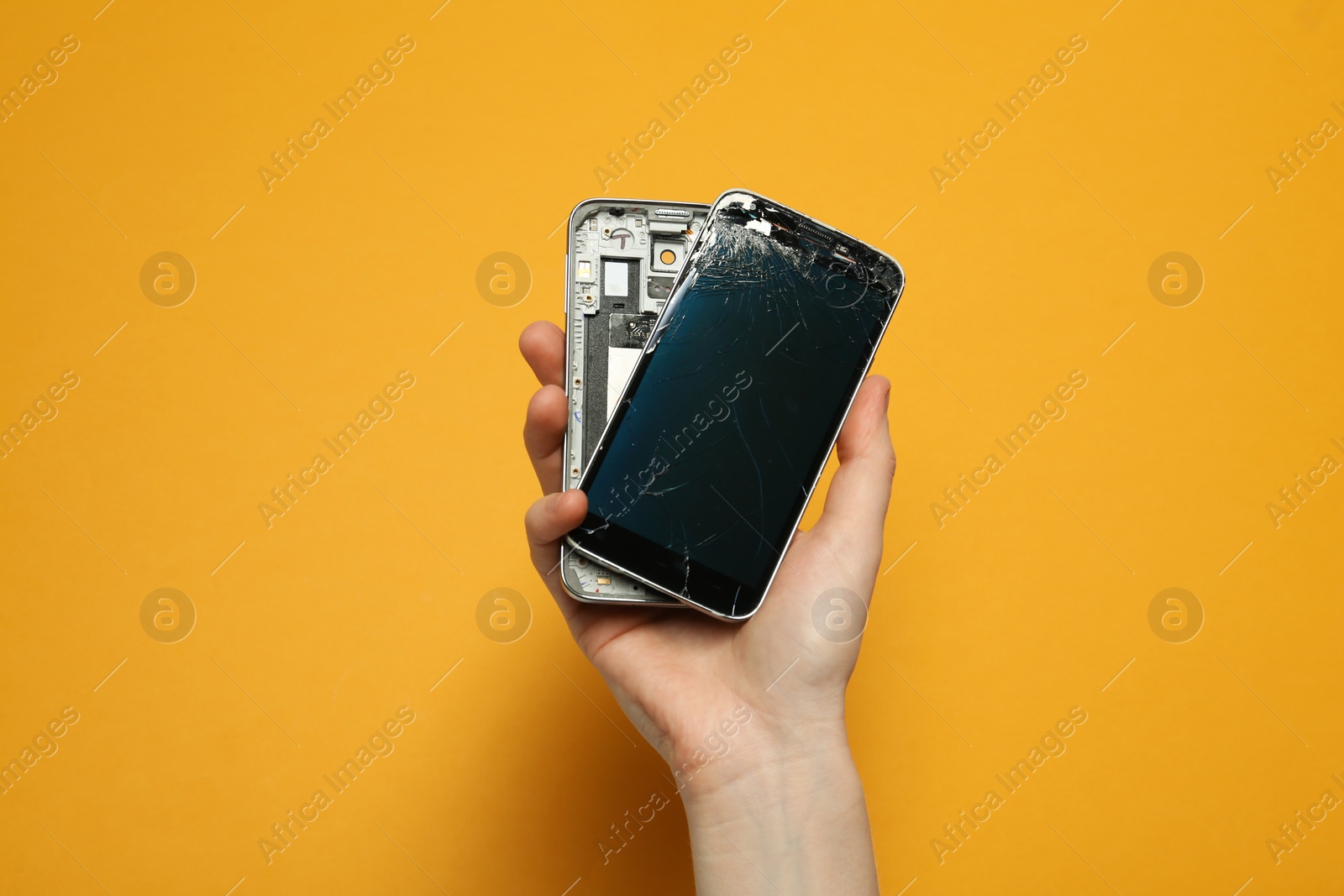 Photo of Woman holding damaged smartphone on orange background, closeup. Device repairing