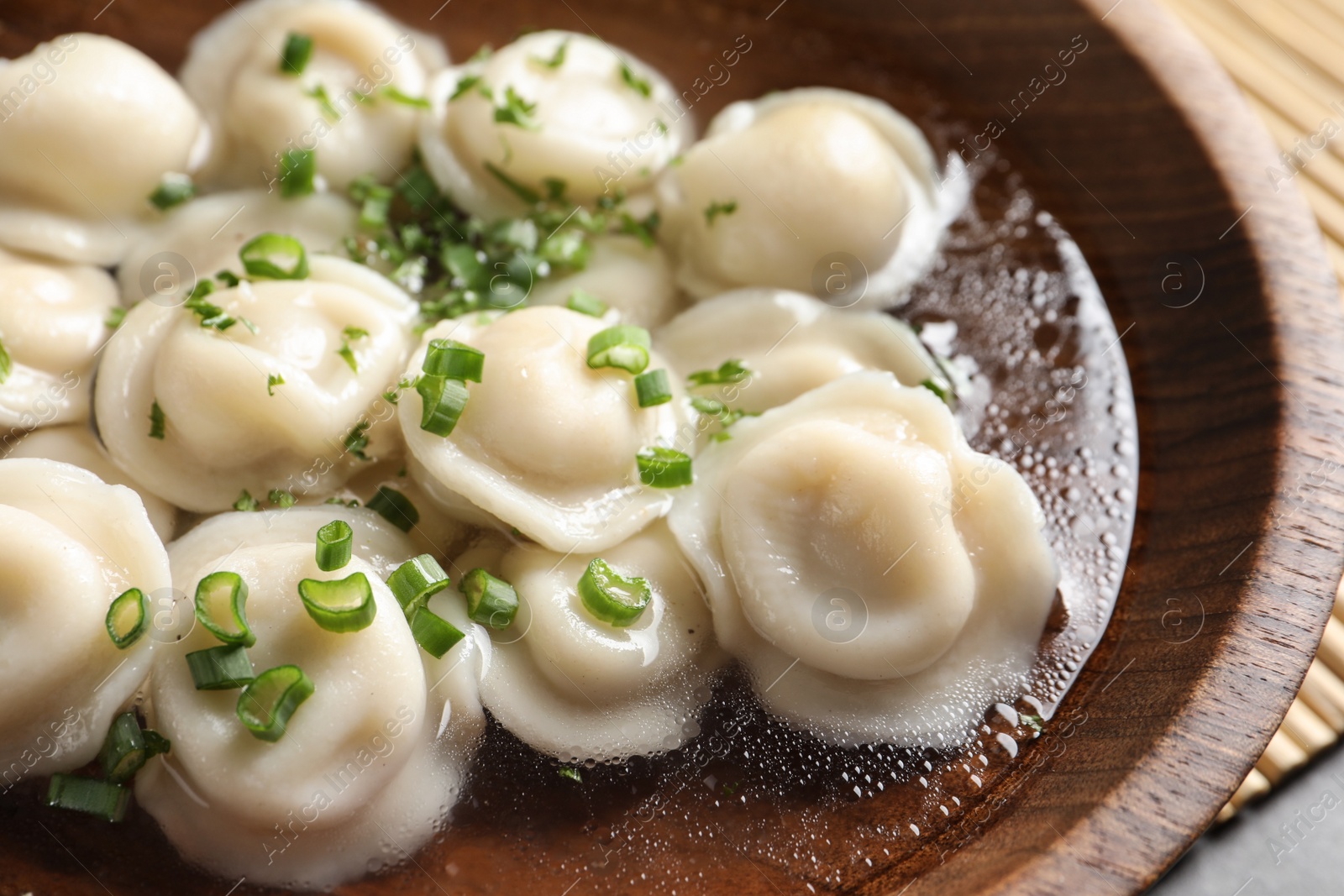 Photo of Bowl of tasty dumplings in broth on table, closeup