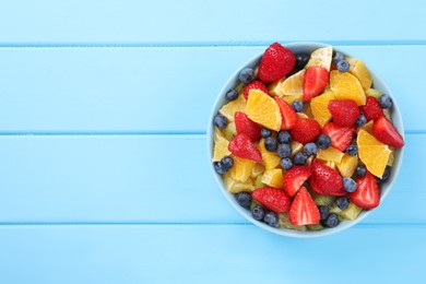 Photo of Delicious fresh fruit salad in bowl on light blue wooden table, top view. Space for text