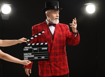 Photo of Senior actor performing role while second assistant camera holding clapperboard on stage, selective focus. Film industry