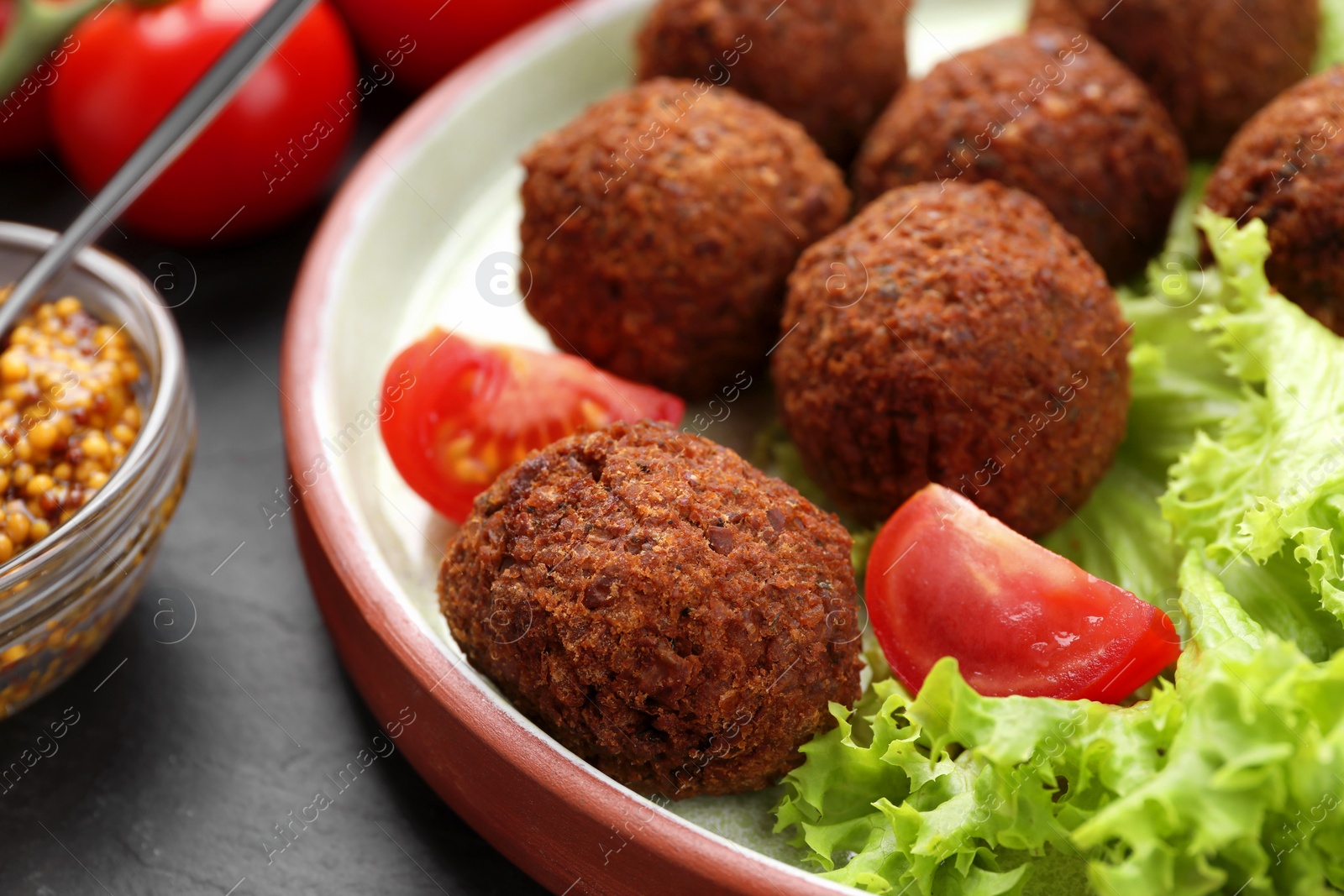 Photo of Delicious falafel balls, tomatoes and lettuce on dark table, closeup. Vegan meat products