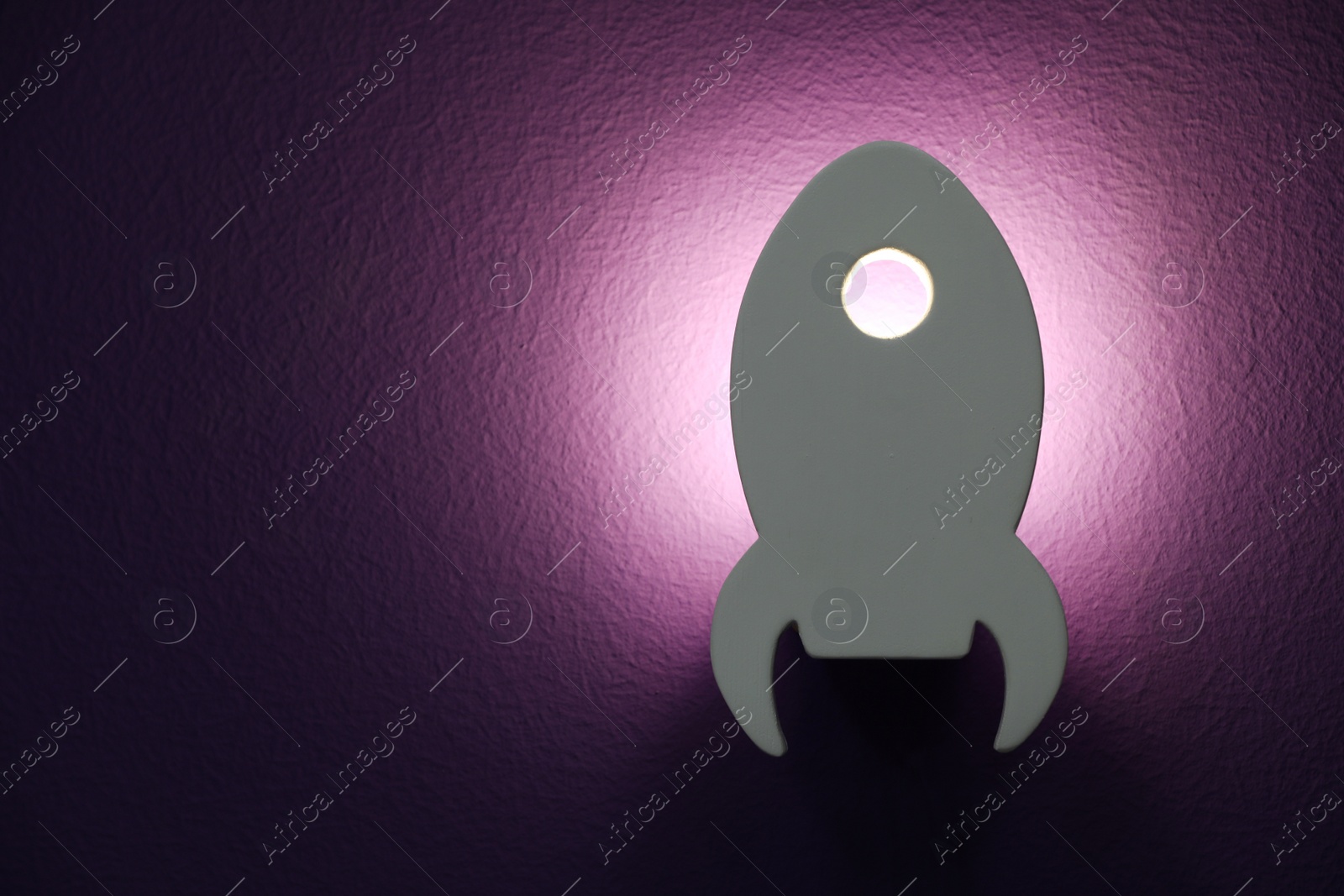 Photo of Rocket shaped night lamp on wall. Space for text