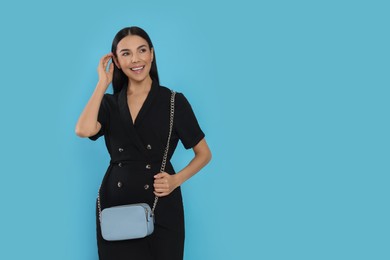 Beautiful young woman with stylish bag on light blue background, space for text