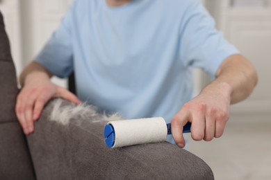 Photo of Pet shedding. Man with lint roller removing dog's hair from armchair at home, closeup