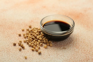 Soy sauce in bowl and beans on beige textured table, closeup