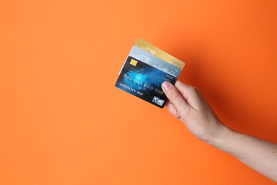 Woman holding credit cards on orange background, closeup