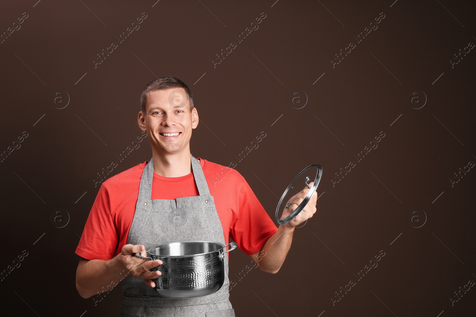 Photo of Happy man with cooking pot on brown background. Space for text