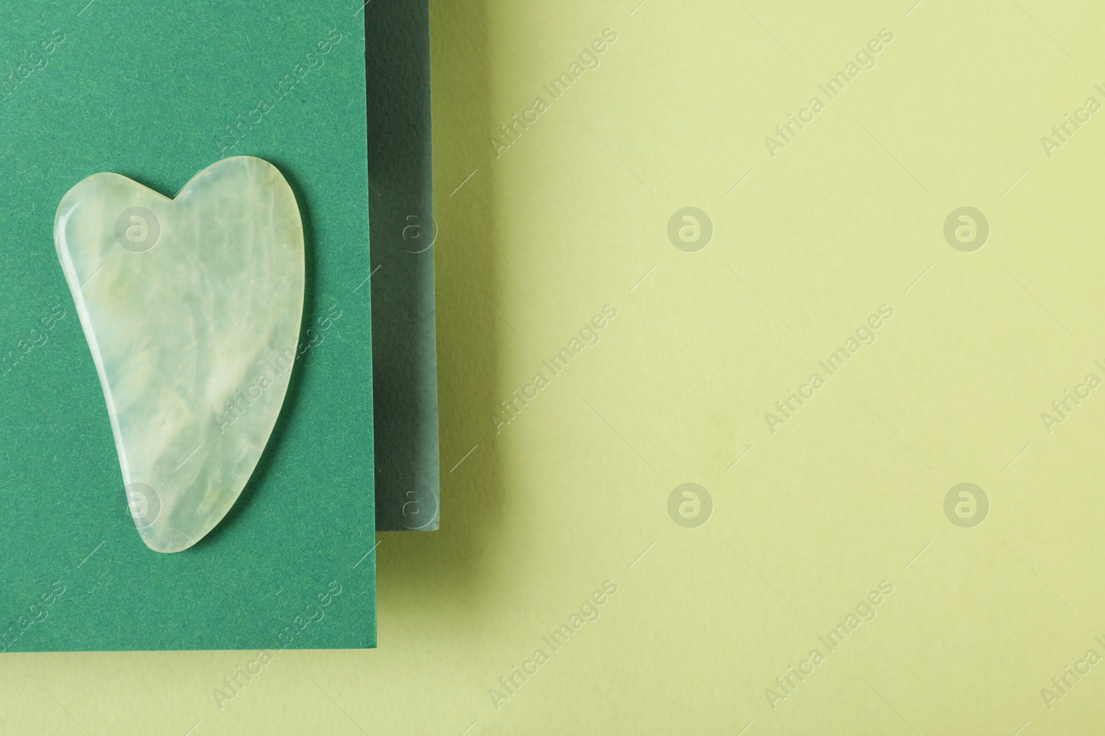 Photo of Jade gua sha tool and paper on green background, top view. Space for text