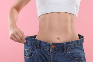 Photo of Slim woman wearing big jeans on pink background, closeup. Weight loss