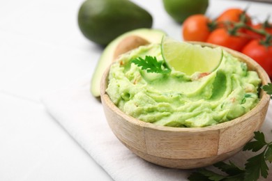 Photo of Bowl of delicious guacamole and ingredients on white table, closeup. Space for text