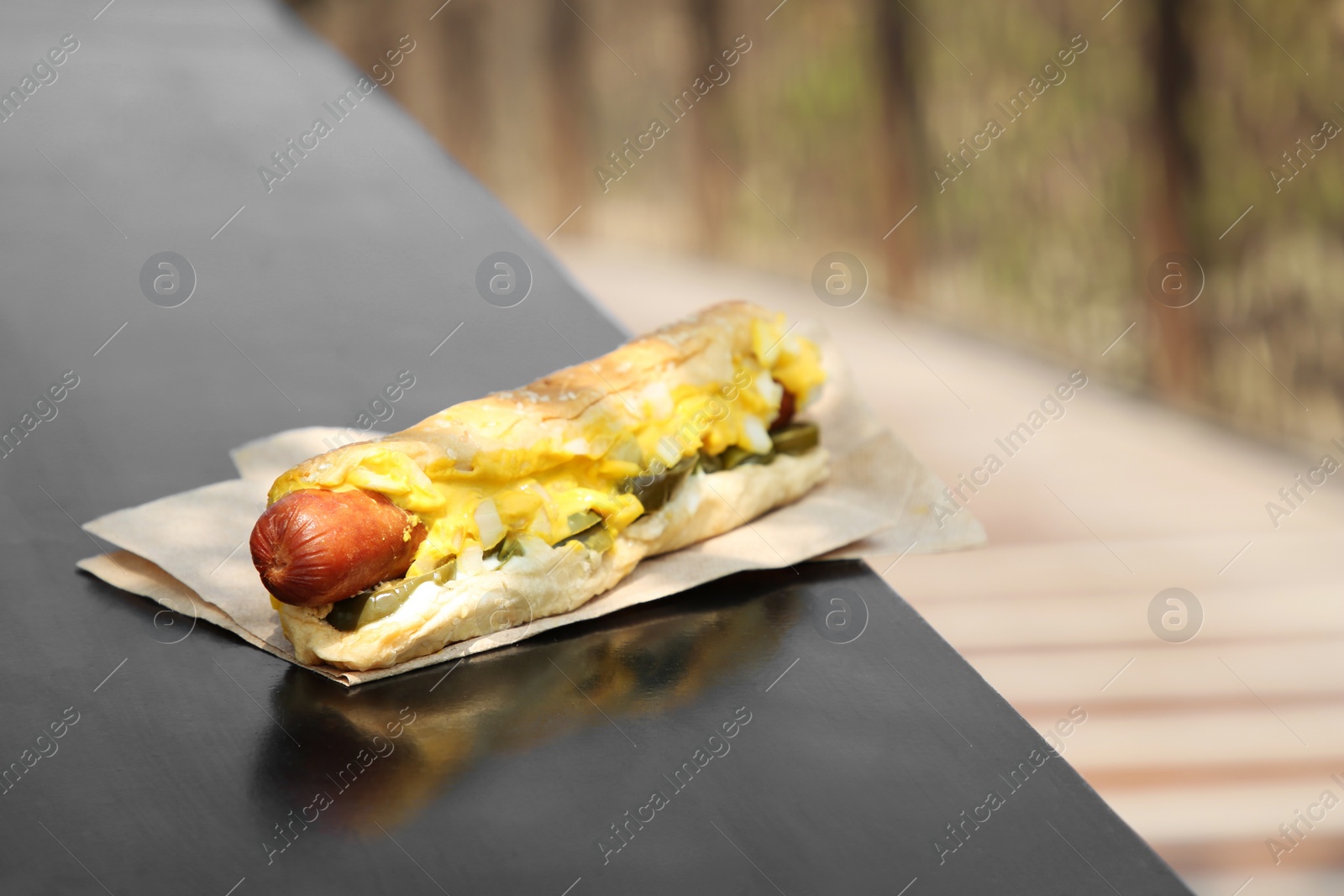 Photo of Fresh tasty hot dog with sauce on dark surface outdoors