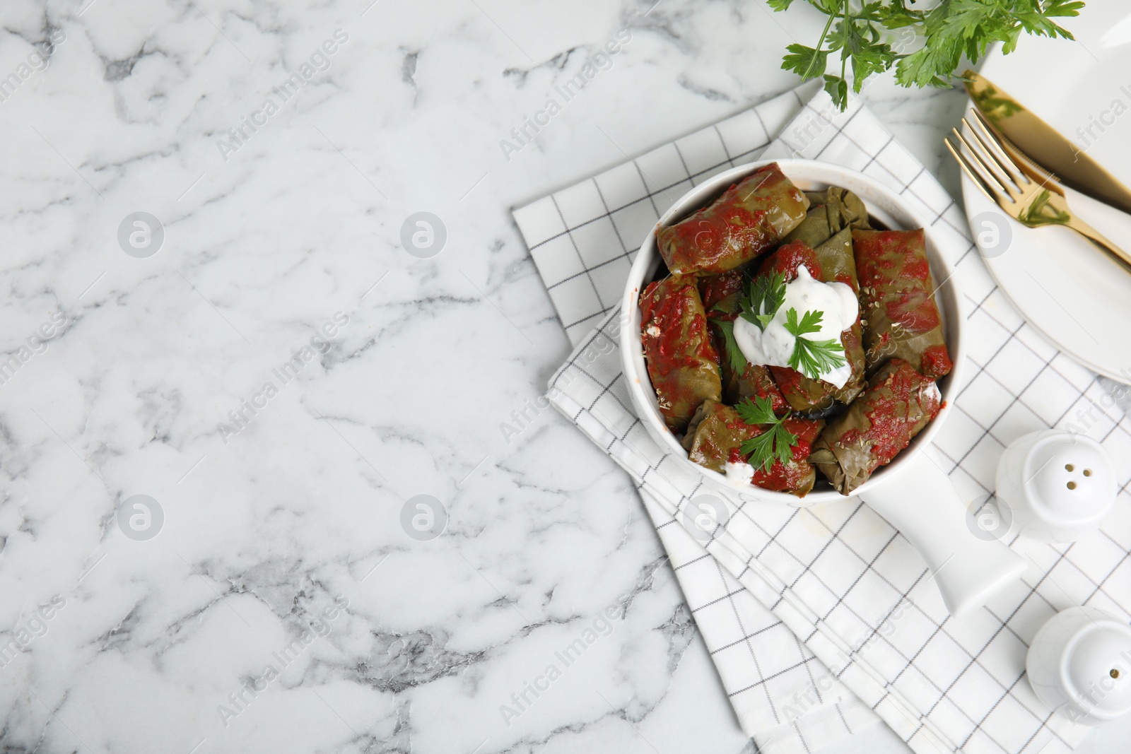 Photo of Delicious stuffed grape leaves with sour cream and tomato sauce on white marble table, flat lay