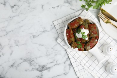 Delicious stuffed grape leaves with sour cream and tomato sauce on white marble table, flat lay