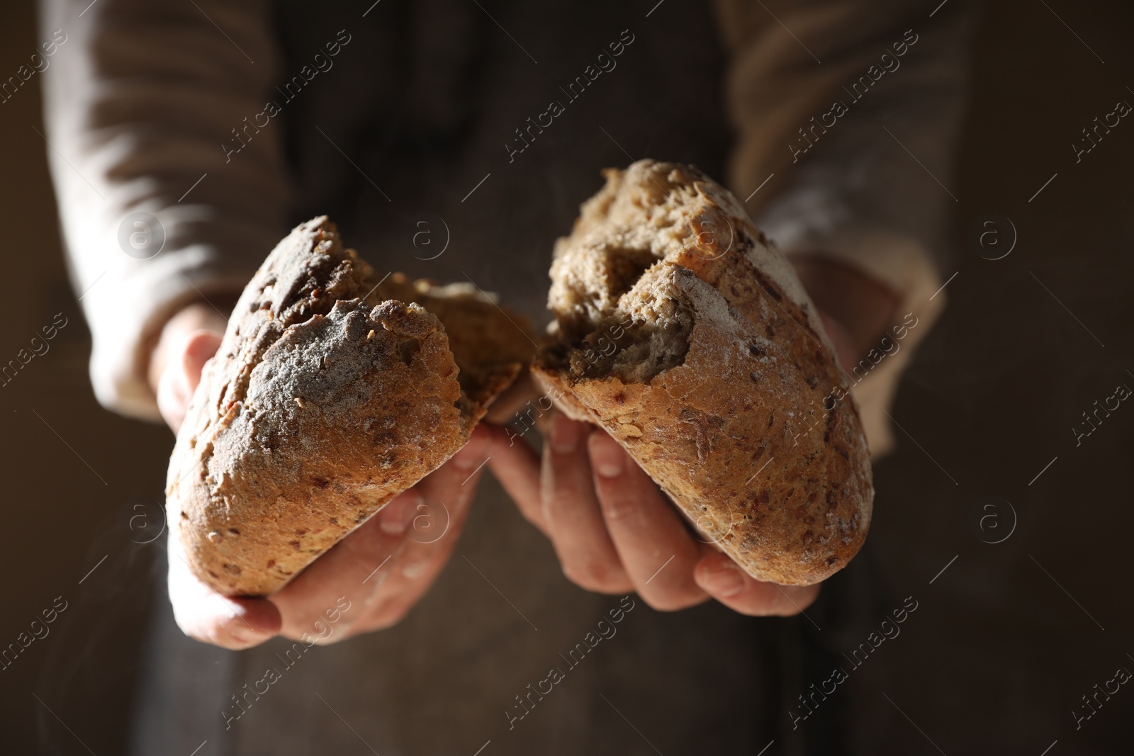 Photo of Man breaking loaf of fresh bread on dark background, closeup