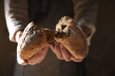 Photo of Man breaking loaf of fresh bread on dark background, closeup