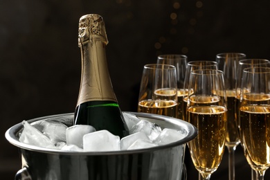 Bottle in bucket with ice near glasses of champagne on dark background